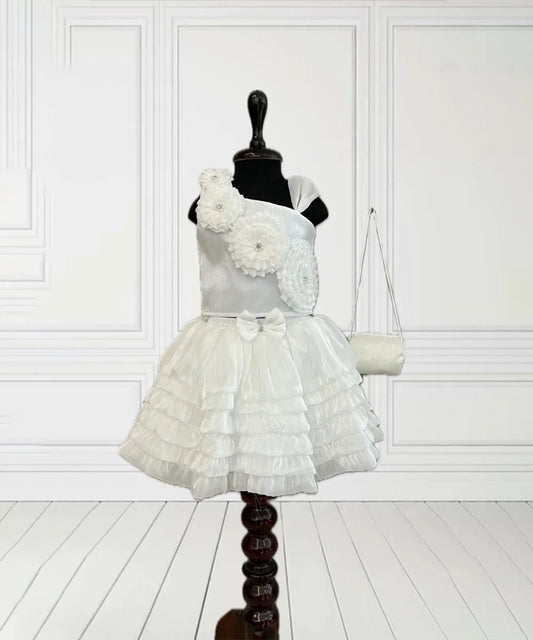 This White Coloured kids birthday wear dress consists of a crop top, a skirt and a matching handbag. It features floral detailing on the top and a cute bow on the waist.