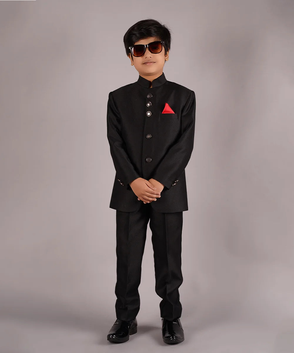 This classic black coloured Jodhpuri suit set is curated from high-quality self-textured fabric. This set has a coat that comes along with matching pants and a red colored pocket square for boys.