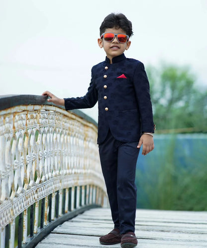 It's a navy blue Colored self-Jacquard design Jodhpuri Suit for Boys. It consists of a Jodhpuri Coat along with matching pants and a red coloured pocket square.