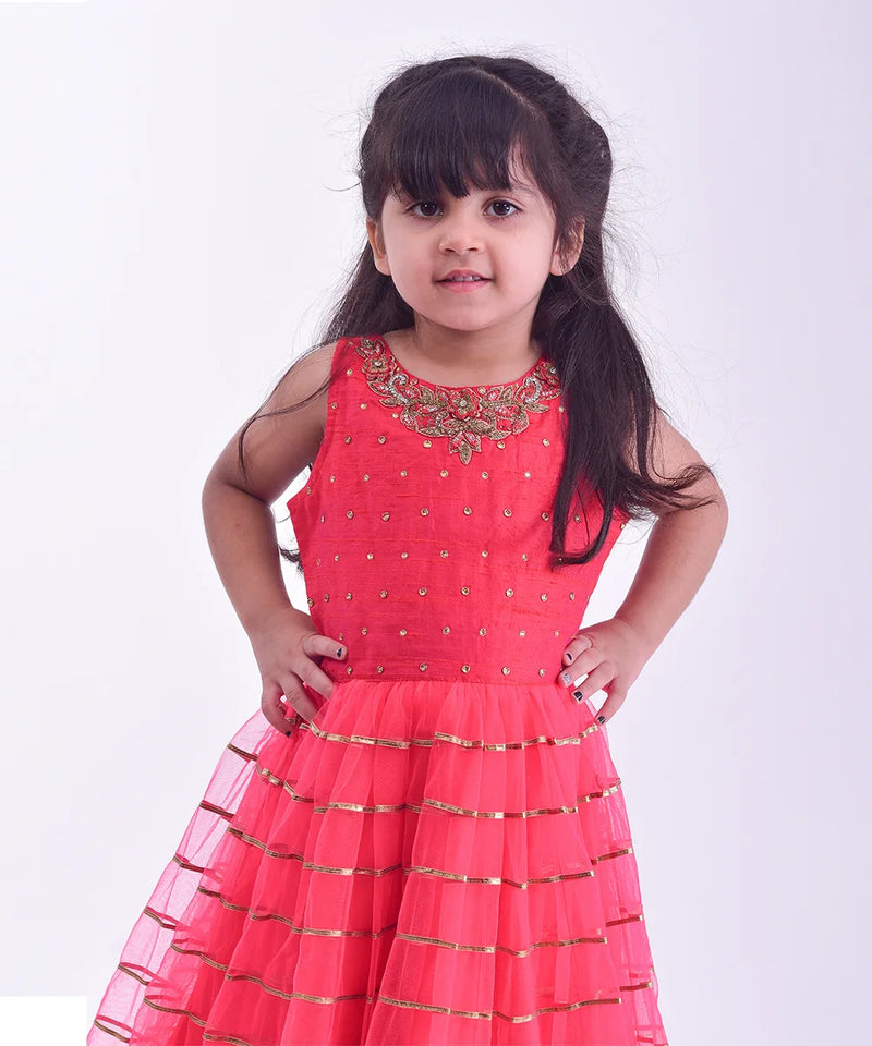 It is an elegant red party gown for girls and comes with short sleeves that can be stitched as per requirement. It features beautiful embroidery work and a matching fabric belt to be tied at the back.