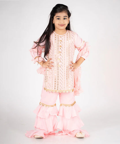 This light pink party wear dress for kids consists of a short embroidered kurta that comes with a back zip closure and a matching sharara. It features lace detailing on sharara and sleeves. Moreover, dupatta comes with the beautiful frill detailing.