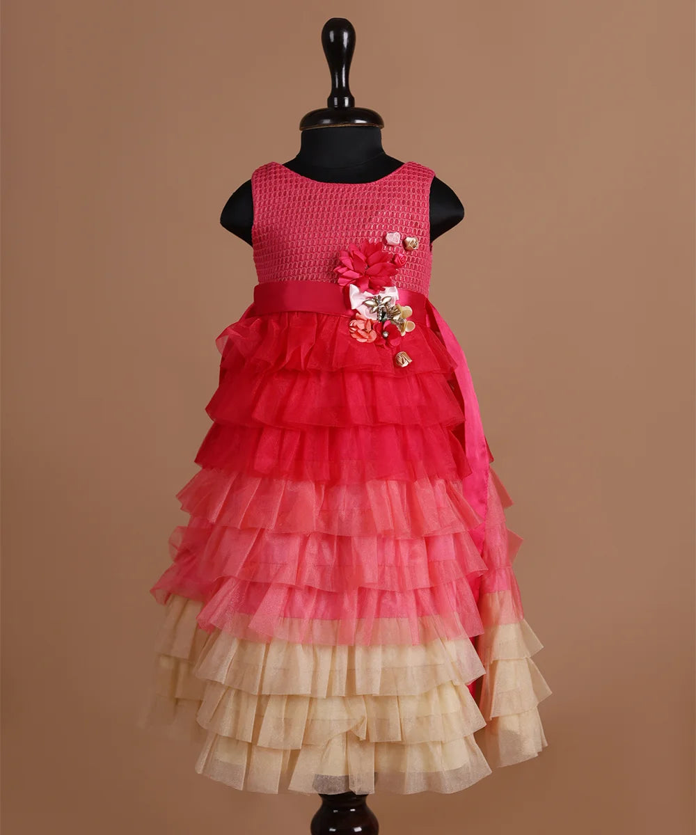 It is a multi Colored frilly gown with a back zip closure. It features flowers with lots of frill detailing and an attached pink Colored belt to be tied at the back.