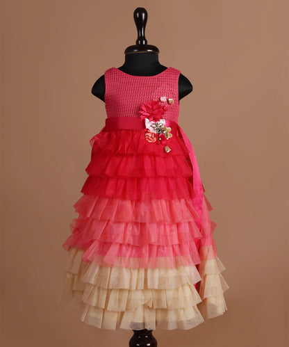 It is a multi Colored frilly gown with a back zip closure. It features flowers with lots of frill detailing and an attached pink Colored belt to be tied at the back.