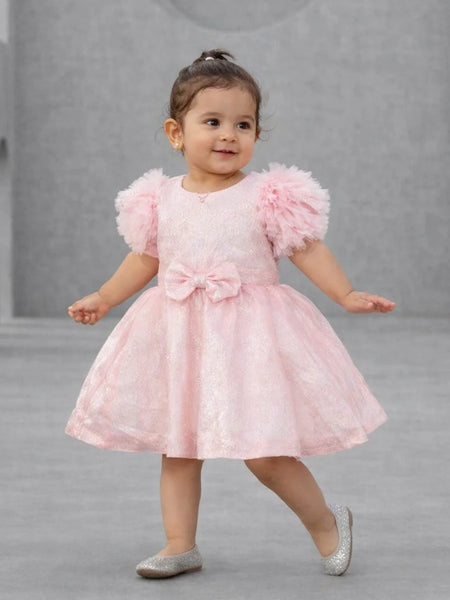 Child wearing a pink dress with fluffy sleeves on a gray background