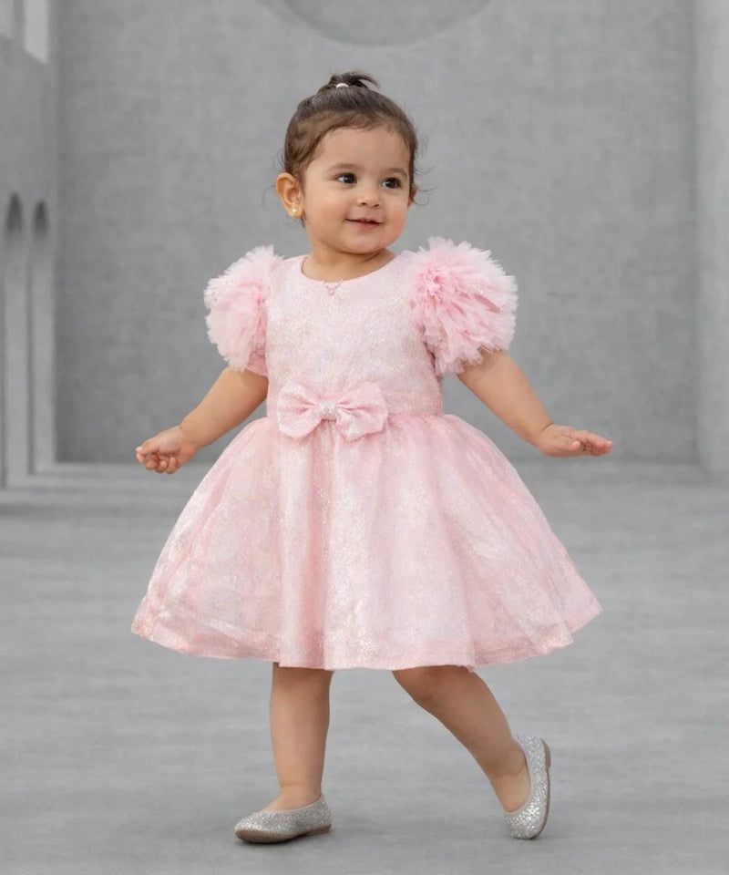 Child wearing a pink dress with fluffy sleeves on a gray background