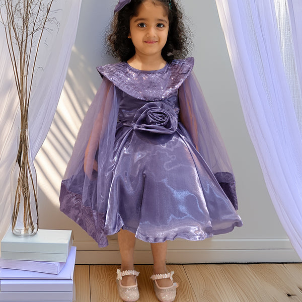 girl in a purple dress with a cape standing indoors.