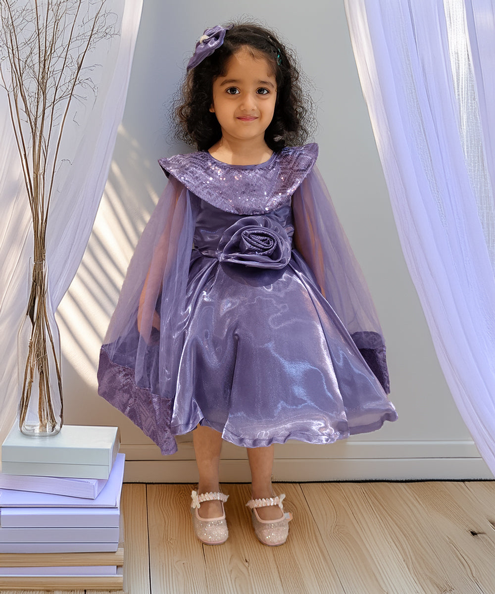 girl in a purple dress with a cape standing indoors.