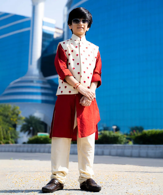 Pick this boys' kurta pajama set for your little kid layered by a sleeveless Nehru collared floral printed jacket. Made from blend fabric, it is a full-sleeved red asymmetric kurta with a cream colored pajama .