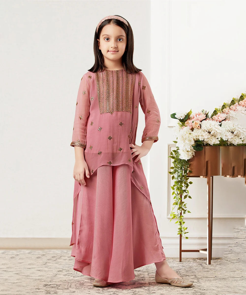 This onion pink sharara set consist of an embroidered high-low kurta, inner and palazzo for your kids with a back zip closure. It features embroidery work on kurta.