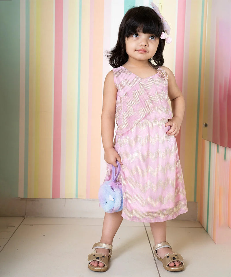 It’s a light pink colored fancy girl dress for weddings with a golden print and an elasticated waist. It features a cute flower attached to the top left side of the dress.