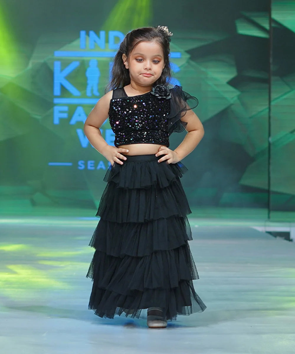 This beautiful black lehenga for kids consist of a sequin crop top that comes with a back zip closure and a layered ruffle Lehenga. It features beautiful big flower on one side of the shoulder.
