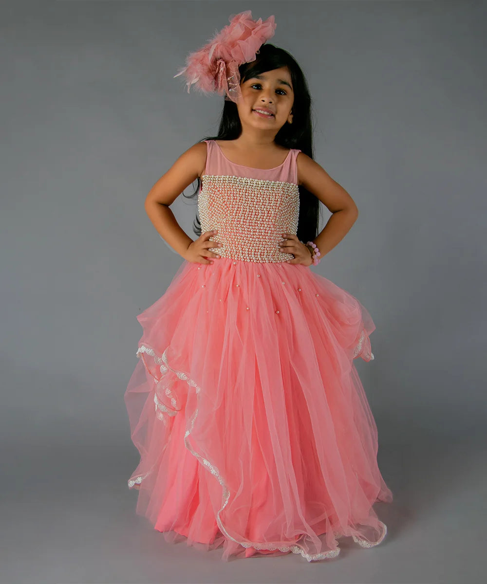 It’s a peach Colored gown for kids that comes with the back zip closure. It features pearl detailing on yoke and comes with the fabric belt to be tied at the back.