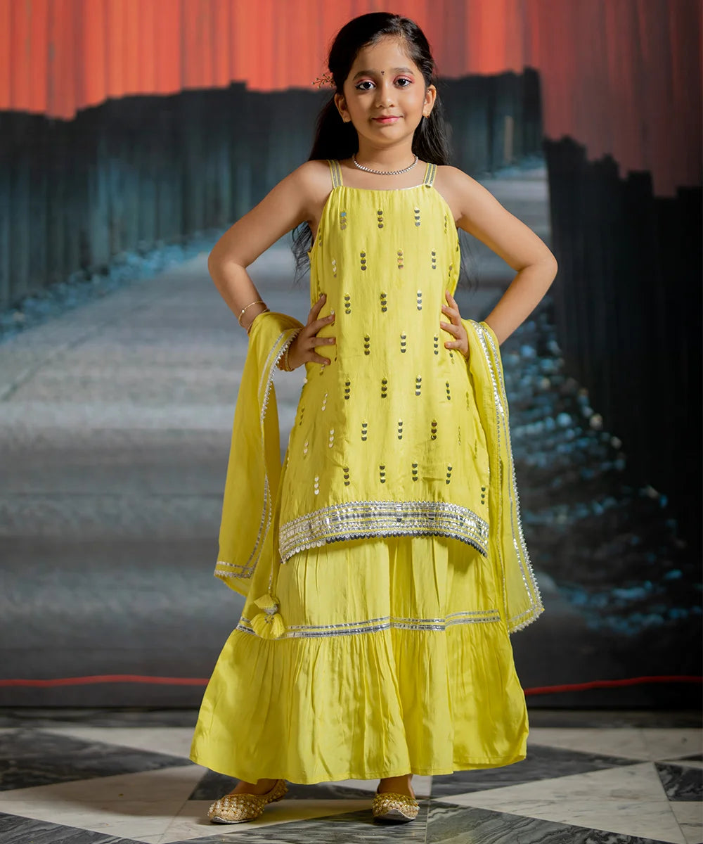 This yellow sharara consist of short kurta that comes with a back zip closure, a sharara and a dupatta. It features mirror work, tassels and lace detailing on kurta. There is beautiful lace detailing done on sharara and dupatta too.