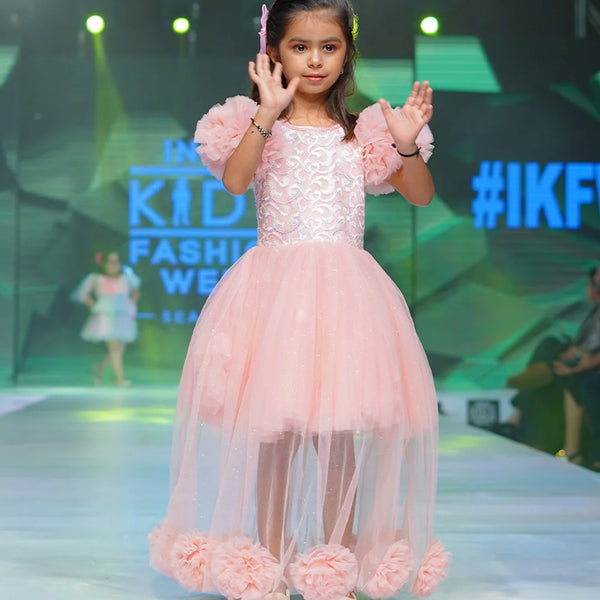 It’s a fancy pink Colored gown for girls that comes with the ruffle sleeves and back zip closure.  It features big flower detailing and the fabric belt to be tied at the back.