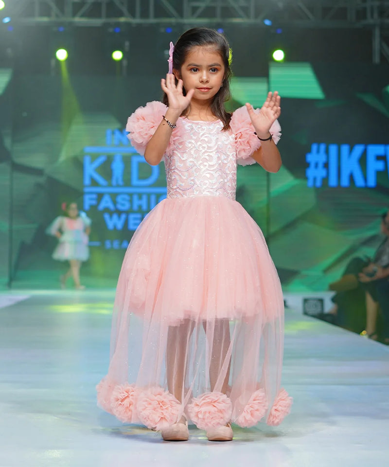 It’s a fancy pink Colored gown for girls that comes with the ruffle sleeves and back zip closure.  It features big flower detailing and the fabric belt to be tied at the back.