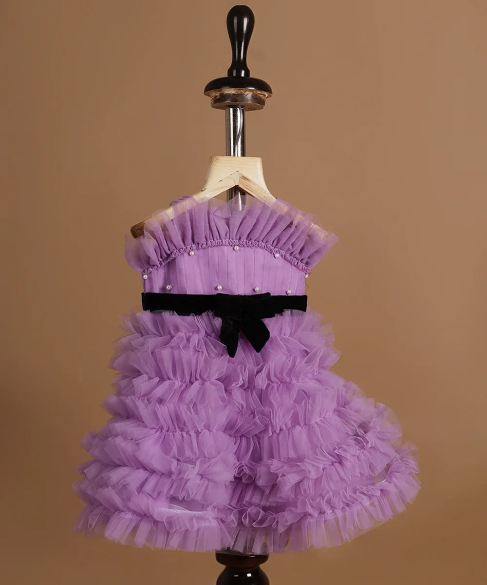 It’s a purple Colored frock with lots of frill and pleated detailing. It features black velvet belt and pearl detailing on the dress.