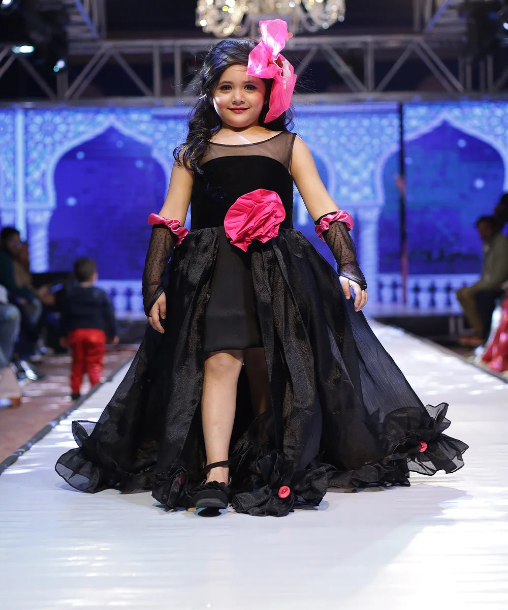It’s a stylish black gown for girls that comes with the back zip closure. It features big flower on the waist and small floral detailing on the ruffles present at the bottom side of the gown.