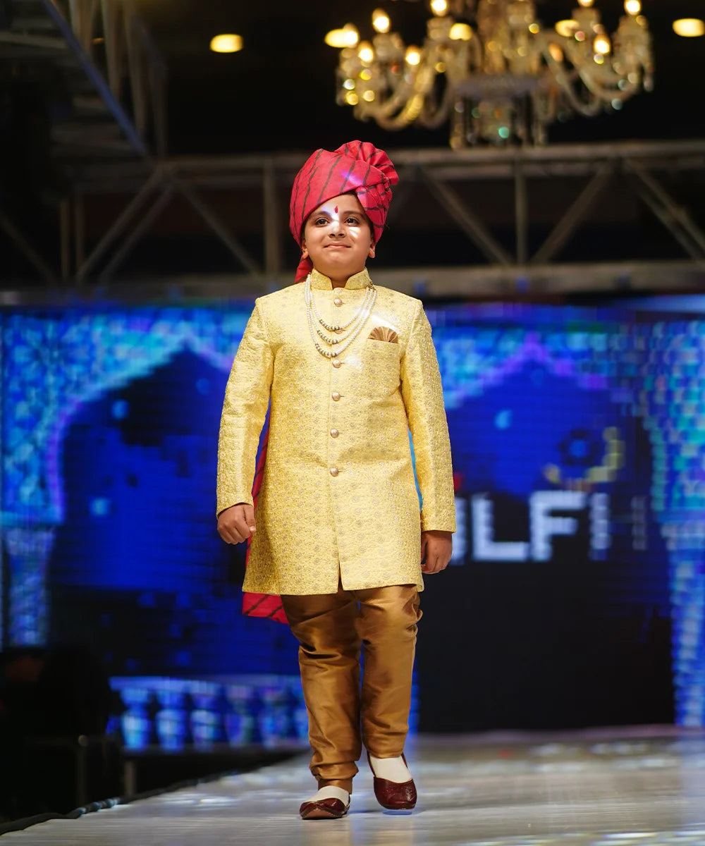 It is a Yellow Jacquard Indo Western Jodhpuri Suit Set for a wedding for boys. It consists of a Sherwani Coat, matching beige breeches pants and a pocket square. 