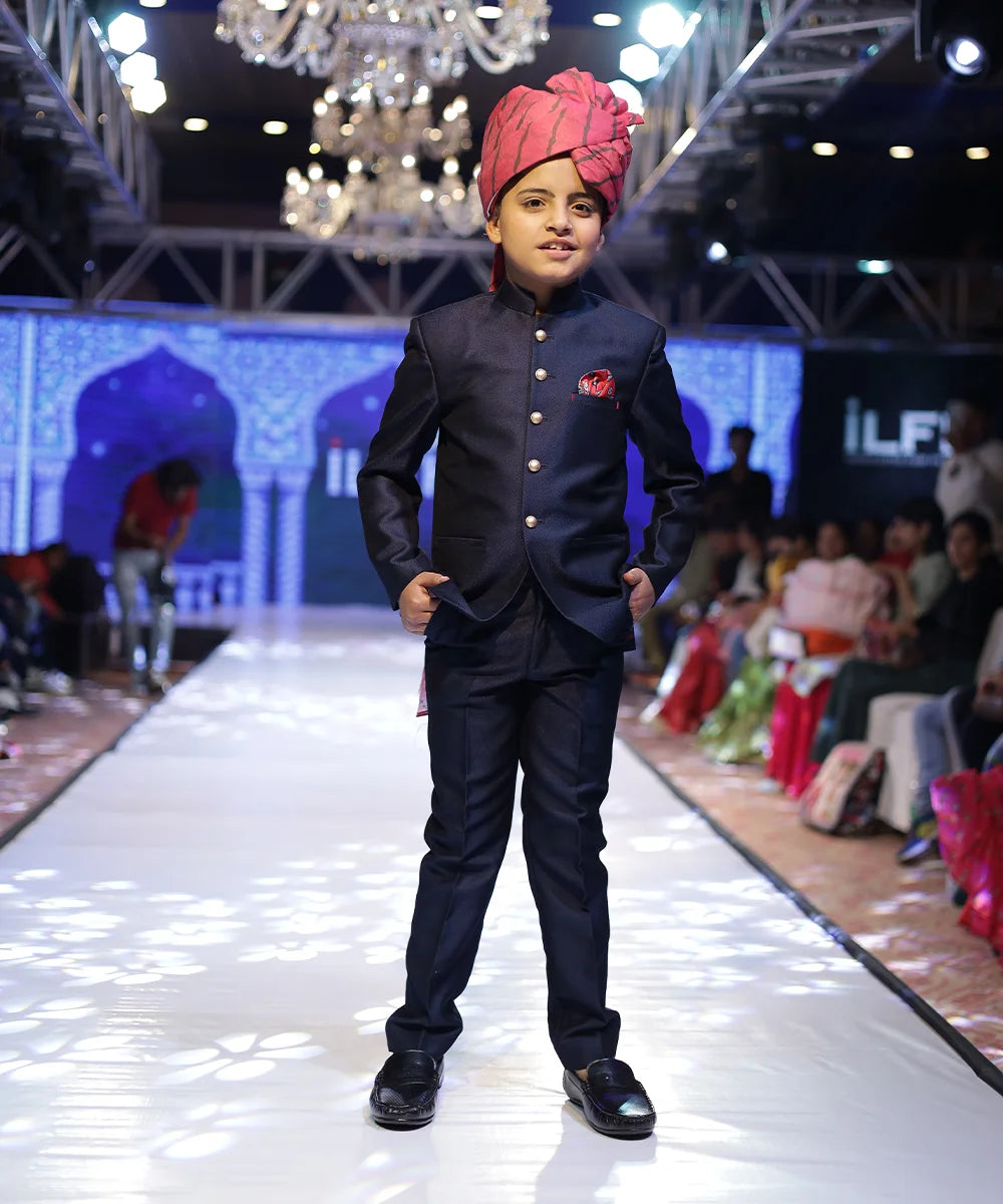 It's a navy blue coloured Jodhpuri suit set that comes with a Nehru collar coat, matching pants and a pink colour printed pocket square. 