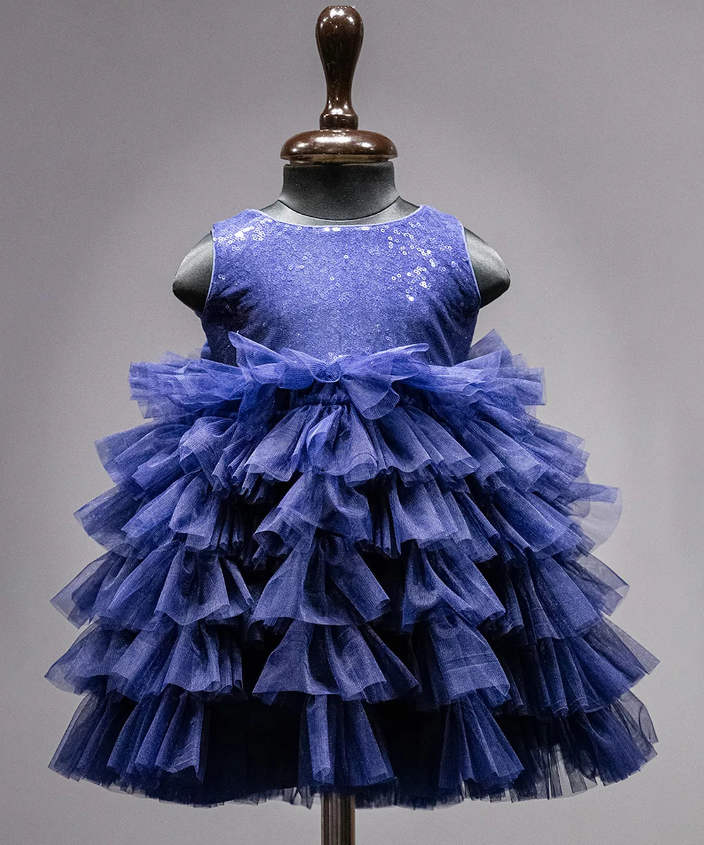 It’s a blue ruffle frock that is paired with a matching hair pin and shoes curated from net and sequin fabric. It’s a trendy dress for kids. It features a big bow at the back of the dress curate from the matching sequin fabric.