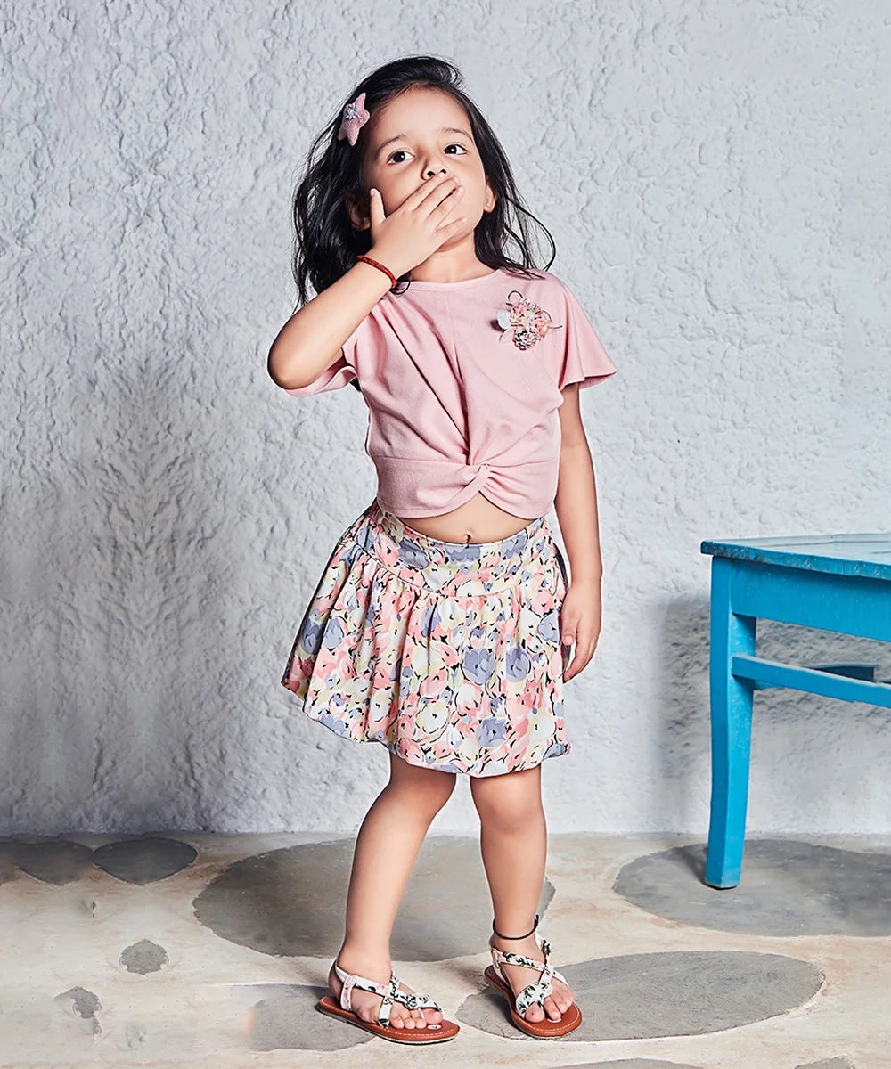 This peach Colored outfit Consists of a top and printed skirt-style shorts for kid girl. The top comes with a front knot and floral broach detailing.