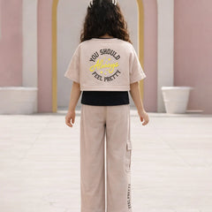 Person wearing a beige t-shirt with text and light-colored pants in an indoor setting.