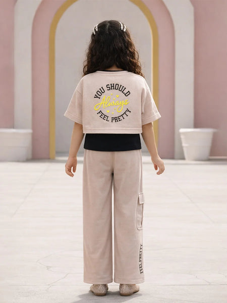 Person wearing a beige t-shirt with text and light-colored pants in an indoor setting.
