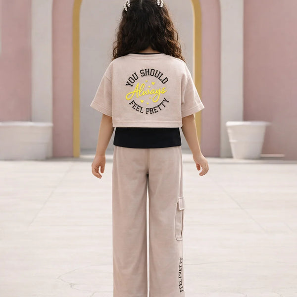 Person wearing a beige t-shirt with text and light-colored pants in an indoor setting.