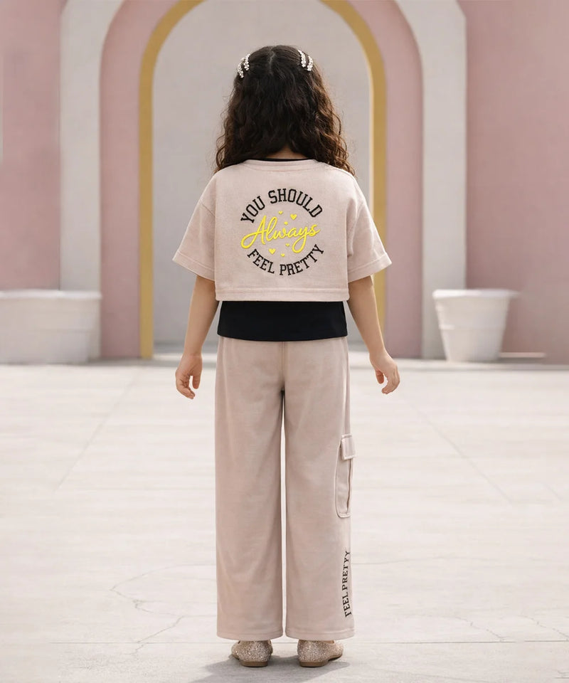 Person wearing a beige t-shirt with text and light-colored pants in an indoor setting.