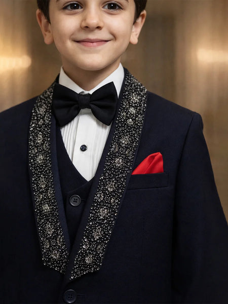 Young boy in a formal tuxedo with a red handkerchief against a warm-toned background
