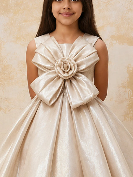 Young girl wearing a beige dress with a large bow and floral detail against a beige background
