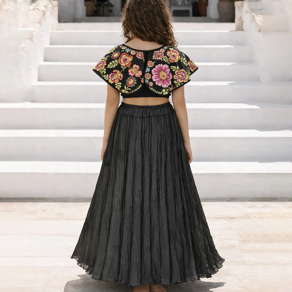 girl wearing a floral top and black pleated skirt on white steps.