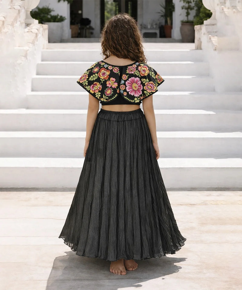 girl wearing a floral top and black pleated skirt on white steps.