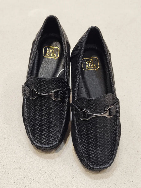 Pair of black woven shoes with a gold logo on a beige background