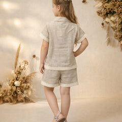 Young girl in a light gray outfit standing in front of floral decorations.