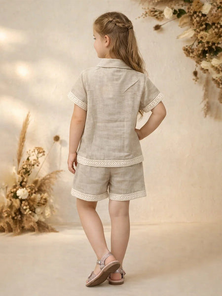 Young girl in a light gray outfit standing in front of floral decorations.
