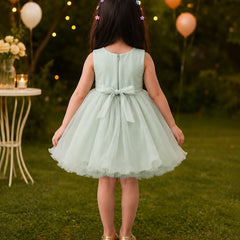 Young girl in a light green dress standing outdoors with balloons and string lights in the background.