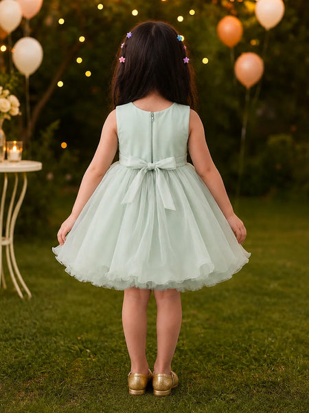Young girl in a light green dress standing outdoors with balloons and string lights in the background.