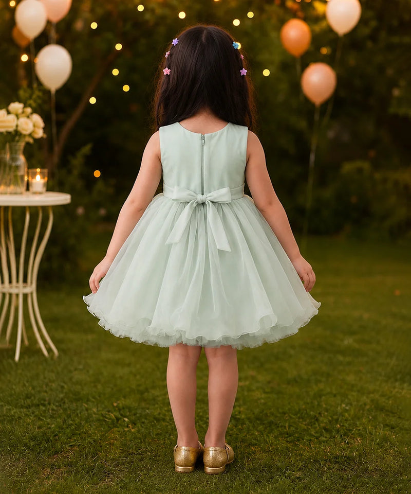 Young girl in a light green dress standing outdoors with balloons and string lights in the background.