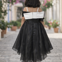 Woman wearing a black and white dress walking on a street with flowers and buildings in the background