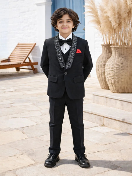 Young boy in a formal black suit with a bow tie standing outdoors.