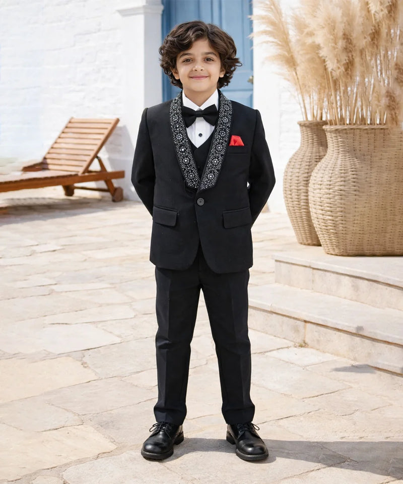 Young boy in a formal black suit with a bow tie standing outdoors.