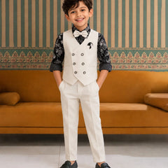 Young boy in a formal outfit standing in a room with a striped wall and orange sofa.