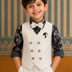 Young boy in a formal outfit with a white vest and bow tie against a decorative wall.