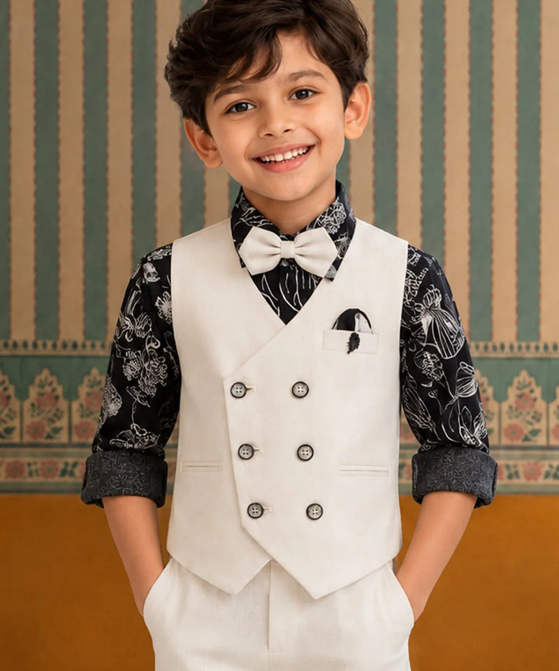 Young boy in a formal outfit with a white vest and bow tie against a decorative wall.