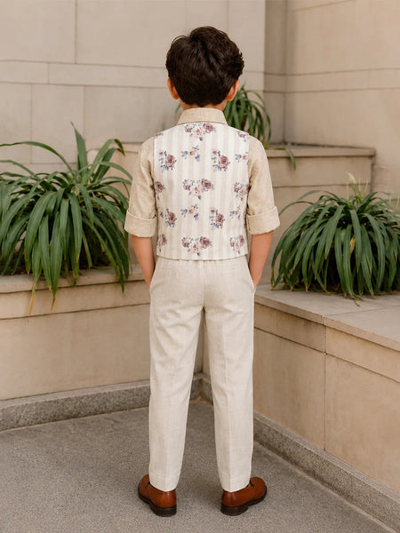 Child wearing a floral vest and beige pants standing in front of a stone wall with plants.