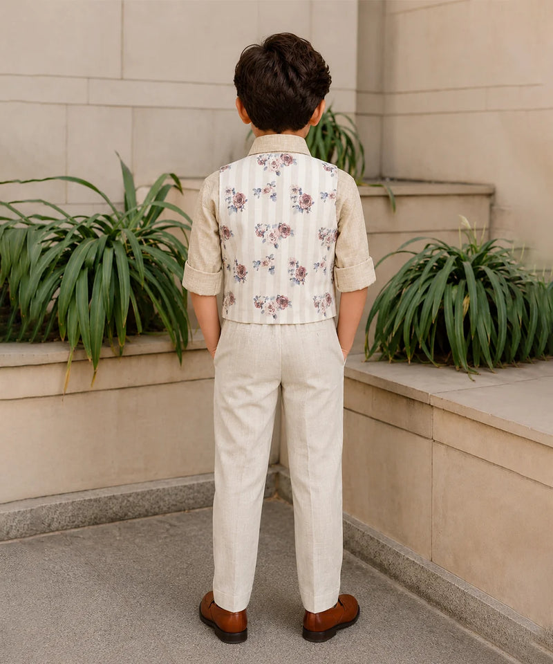Child wearing a floral vest and beige pants standing in front of a stone wall with plants.