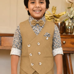 Child wearing a formal outfit with a vest and bow tie, standing in front of a wooden table with decorative items.