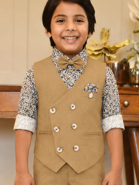 Child wearing a formal outfit with a vest and bow tie, standing in front of a wooden table with decorative items.