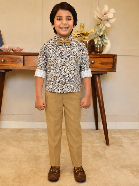 Child wearing a patterned shirt and beige pants standing in a room with wooden furniture and decorative items.